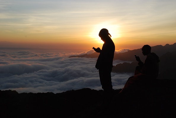 Tanzanian porters and guides stand on a rock half way up Kilimanjaro at sunset in September 2014 trying to get a mobile phone signal to call their wives. Photo credit: PETER MARTELL/AFP/Getty Images